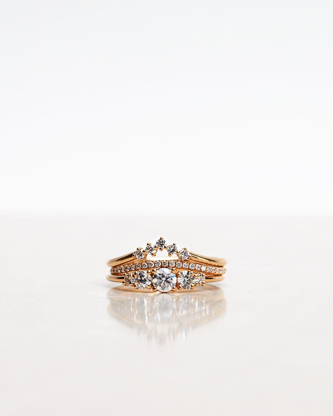 Ring stack with three Mumbaistockholm Fine Jewelry Rings:  Elise Ring in 18K yellow gold with five white, conflict-free diamonds, Jade Petite Wave Half Ring with a curved band half covered with 0.005 CT diamonds TWVS, and Five Diamond Triangle Ring with five 0.02 CT diamonds TWVS.